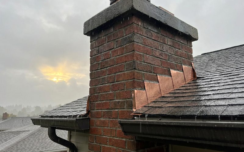 Newly sealed chimney flashing shedding rain on a residential roof